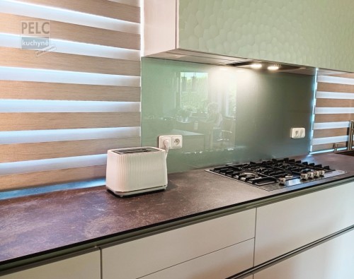 Pohled na pracovní desku s plynovou varnou deskou značky De Dietrich a bílým toastovačem, zástěna z kaleného skla, lakovné sklo s perleťovým lakem.
